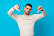 © luismolinero - Young man over isolated blue background showing thumb down
