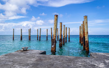 Rusty Poles In Ruins Of Old Pier In Beautiful Blue Water

