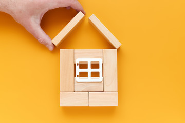 Hand builds a house of wooden blocks on a yellow background. housing, family, construction concept