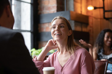 Happy Caucasian millennial girl sit in cafe talking having fun with male friend or colleague during coffee break, smiling young woman meeting on date with guy in coffeehouse, flirting and chatting