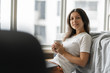 © Kate - Beautiful young brunette girl working on a laptop and drinking coffee, sitting on the floor near the bed by the panoramic window. A cozy workplace. Shopping on the Internet.