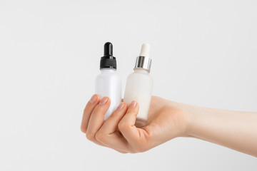 Hands of a beautiful woman hold two serum collagen moisturizer of face into clear white bottle soft light, grey background.