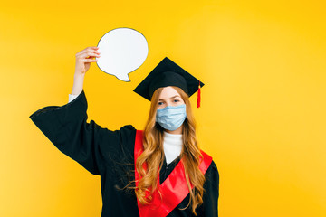 Wall Mural - beautiful graduate with a medical protective mask on her face and a speech bubble on a yellow background. Distance learning, quarantine, coronavirus