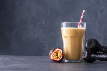 Wall Mural - Fruit protein shake on concrete background. Fresh milkshake with passion fruit. A glass of protein shake with dumbbells.