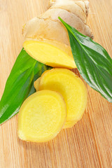 Sliced ​​ginger root and green leaves on a wooden board. The concept of a healthy food, a cure for the common cold, flavoring. Close-up.