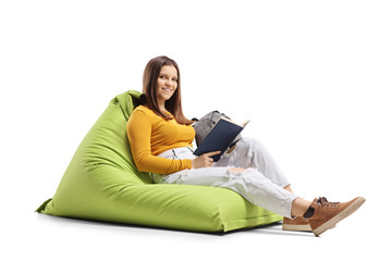 Young woman sitting on a green beanbag with a book and smiling at the camera