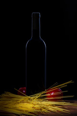 Bottle of wine, two tomatoes, spaghetti pasta on a cutting board on a black background.