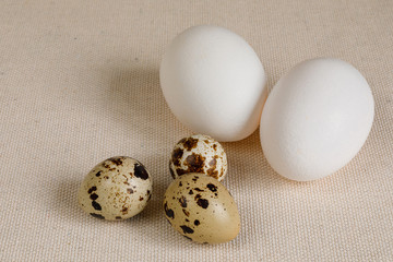 two white chicken eggs and three small quail eggs on a textile napkin.