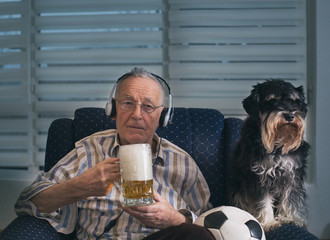 Wall Mural - Old man with dog drinking beer and watching football game