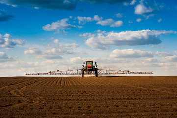 Fototapete - self-propelled sprayer with long arms, fertilizer spreader that fertilizes farm fields view with beautiful clouds.