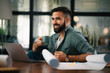 © JustLife - Handsome man drinking coffee in office. Young man working on project.
