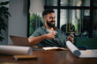 © JustLife - Handsome man drinking coffee in office. Young man working on project.