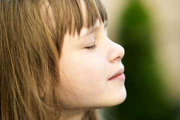 Canvas Print - Portrait of young pretty child girl with long hair enjoying warm sunny day in summer outdoors. Cute female kid relaxing on fresh air outside.