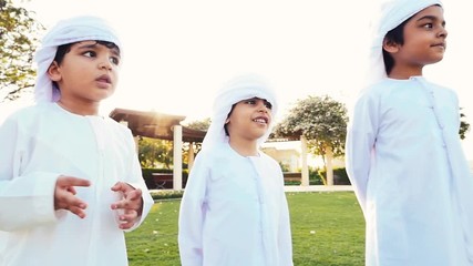 Wall Mural - Kids playing outdoor on the meadow. Children wearing traditional united arab emirates kandura having fun