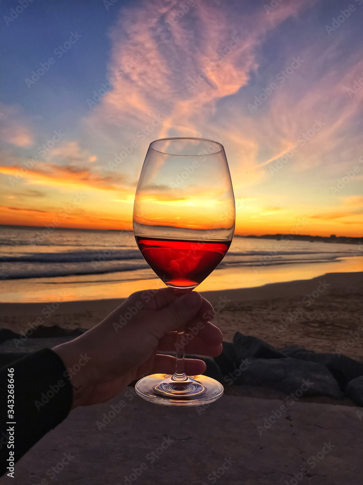 Woman man hand with a glass of red wine on a background of sunset sky and  waves on the beach by the ocean in Portugal Stock Photo | Adobe Stock