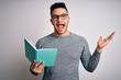 © Krakenimages.com - Young handsome smart student man reading book over isolated white background very happy and excited, winner expression celebrating victory screaming with big smile and raised hands