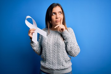 Poster - Young blonde woman holding cancer awareness and stop women violence white ribbon serious face thinking about question, very confused idea