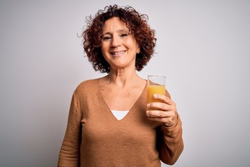 Poster - Middle age curly hair woman drinking healthy glass of orange juice over white background with a happy face standing and smiling with a confident smile showing teeth