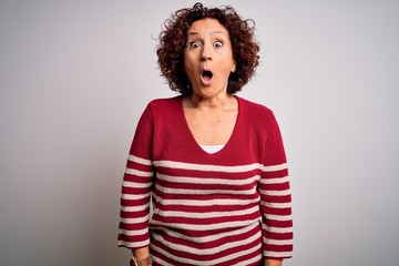 Poster - Middle age beautiful curly hair woman wearing casual striped sweater over white background afraid and shocked with surprise expression, fear and excited face.