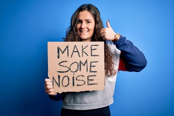 Sticker - Beautiful activist woman holding banner with make some noise message over blue background happy with big smile doing ok sign, thumb up with fingers, excellent sign