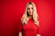 © Krakenimages.com - Young beautiful blonde woman wearing casual t-shirt standing over isolated red background Relaxed with serious expression on face. Simple and natural looking at the camera.