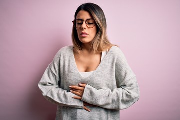 Sticker - Young beautiful brunette woman wearing casual sweater and glasses over pink background with hand on stomach because indigestion, painful illness feeling unwell. Ache concept.