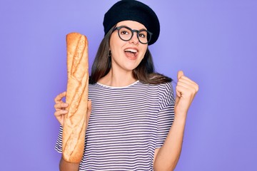 Poster - Young beautiful girl wearing fashion french beret holding fresh baked bread baguette screaming proud and celebrating victory and success very excited, cheering emotion