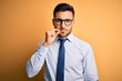 © Krakenimages.com - Young handsome businessman wearing tie and glasses standing over yellow background mouth and lips shut as zip with fingers. Secret and silent, taboo talking