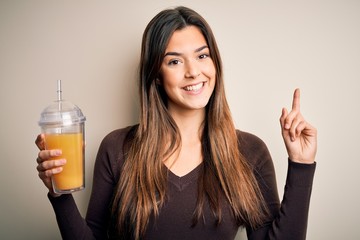 Sticker - Young beautiful girl drinking glass of healthy orange juice over isolated white background surprised with an idea or question pointing finger with happy face, number one