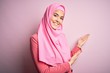 © Krakenimages.com - Young beautiful girl wearing muslim hijab standing over isolated pink background Inviting to enter smiling natural with open hand