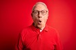 © Krakenimages.com - Grey haired senior man wearing glasses and casual t-shirt over red background afraid and shocked with surprise expression, fear and excited face.