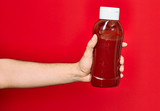 Fototapeta Młodzieżowe - Beautiful hand of man holding bottle with hetchup sauce over isolated red background