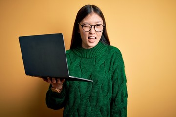 Sticker - Young asian business woman wearing glasses and working using computer laptop winking looking at the camera with sexy expression, cheerful and happy face.