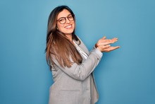 Young Hispanic Business Woman Wearing Glasses Standing Over Blue Isolated Background Pointing Aside With Hands Open Palms Showing Copy Space, Presenting Advertisement Smiling Excited Happy