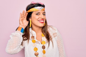 Canvas Print - Young hispanic hippie woman wearing fashion boho style and sunglasses over pink background smiling with hand over ear listening an hearing to rumor or gossip. Deafness concept.