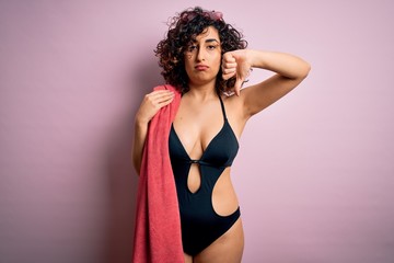 Sticker - Young beautiful curly arab woman on vacation wearing swimsuit holding beach towel with angry face, negative sign showing dislike with thumbs down, rejection concept