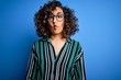 © Krakenimages.com - Young beautiful curly arab woman wearing striped shirt and glasses over blue background making fish face with lips, crazy and comical gesture. Funny expression.