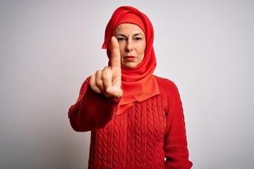 Wall Mural - Middle age brunette woman wearing muslim traditional hijab over isolated white background Pointing with finger up and angry expression, showing no gesture