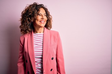 Middle age beautiful businesswoman wearing elegant jacket over isolated pink background looking away to side with smile on face, natural expression. Laughing confident.