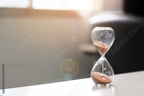 Cuadros en Lienzo Hourglass on table office with copy space, Sand flowing through the bulb of Sandglass measuring the passing time