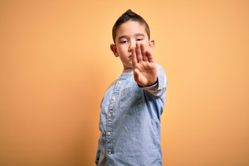 Poster - Young little boy kid wearing elegant shirt standing over yellow isolated background doing stop sing with palm of the hand. Warning expression with negative and serious gesture on the face.