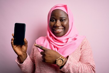 Sticker - African american plus size woman wearing muslim hijab holding smartphone showing screen very happy pointing with hand and finger