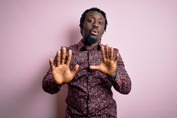 Poster - Young handsome african american man wearing casual shirt standing over pink background Moving away hands palms showing refusal and denial with afraid and disgusting expression. Stop and forbidden.