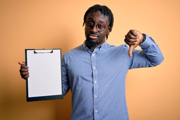 Young african american inspector man wearing glasses holding clipboard checklist with angry face, negative sign showing dislike with thumbs down, rejection concept