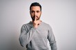 © Krakenimages.com - Young handsome man with beard wearing casual sweater standing over white background asking to be quiet with finger on lips. Silence and secret concept.