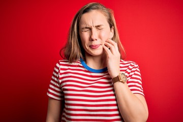 Sticker - Young beautiful blonde woman wearing casual striped t-shirt over isolated red background touching mouth with hand with painful expression because of toothache or dental illness on teeth. Dentist