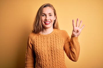 Sticker - Young beautiful blonde woman wearing casual sweater standing over yellow background showing and pointing up with fingers number four while smiling confident and happy.