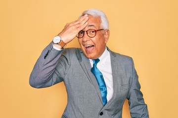 Canvas Print - Middle age senior grey-haired handsome business man wearing glasses over yellow background surprised with hand on head for mistake, remember error. Forgot, bad memory concept.