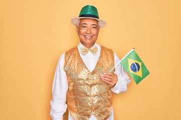 Wall Mural - Middle age senior grey-haired man wearing Brazilian carnival custome holding Brazil flag with a happy face standing and smiling with a confident smile showing teeth