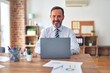 © Krakenimages.com - Middle age handsome businessman wearing tie sitting using laptop at the office with a happy and cool smile on face. Lucky person.